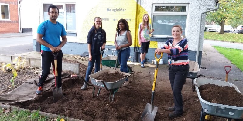 Group of students with shovels and wheelbarrows creating green space